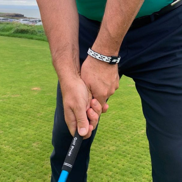 Close-up of a golfer's grip on the green, wearing the AV Edge Legend White/Black frequency wristband, demonstrating how the HEF Technology might support biomechanical stability and potentially increase clubhead speed through improved energy field alignment and focus.