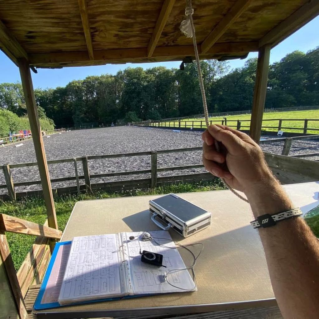 International dressage judge and trainer Alex Gingell wearing the AV Edge Legend White/Black frequency wristband while officiating at an outdoor arena, demonstrating how the HEF Technology might support sustained focus, mental clarity, and posture during long days of high-level judging, offering a non-invasive solution for peak concentration.