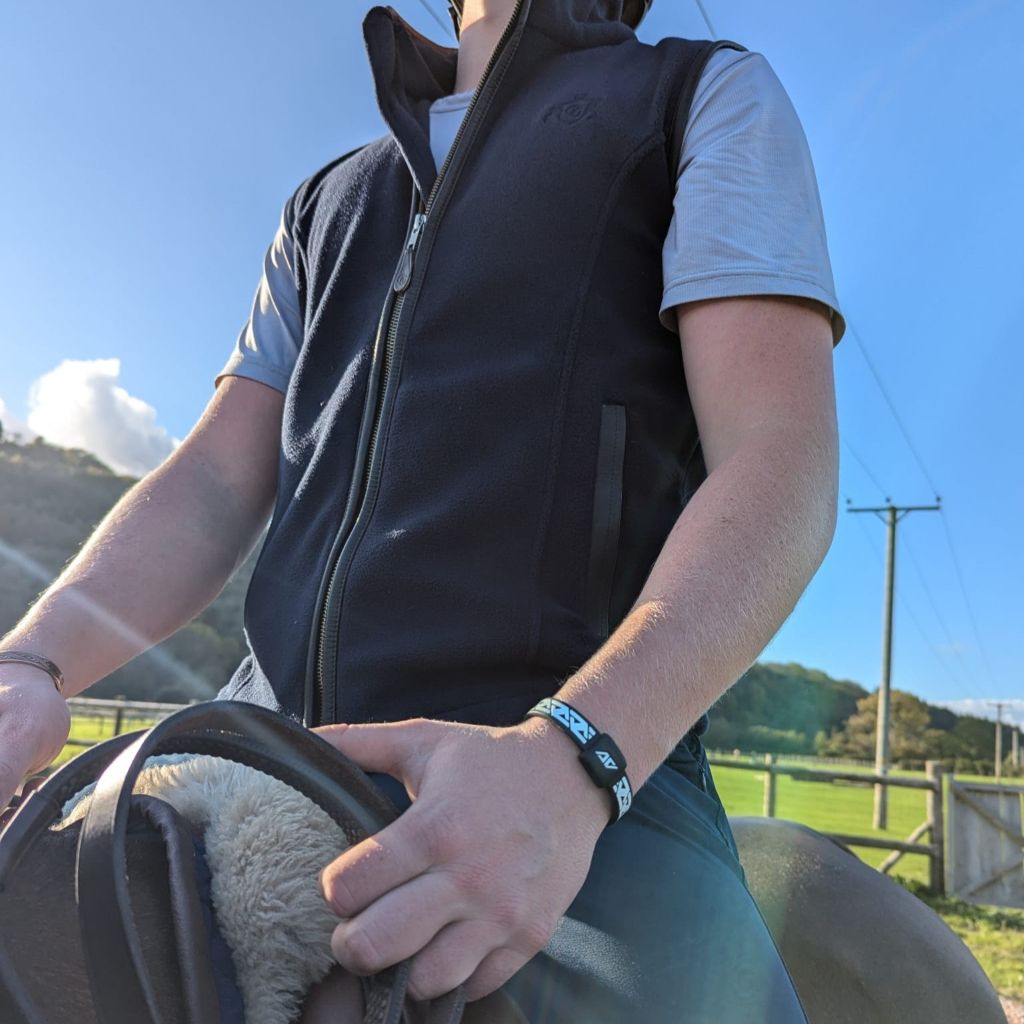 Low-angle view of competitive rider Archie Cloke on horseback, wearing his AV Edge Legend White/Black frequency wristband, demonstrating how the HEF Technology might support biomechanical stability, focus, and posture for enhanced rider performance and confidence during demanding equestrian activities.
