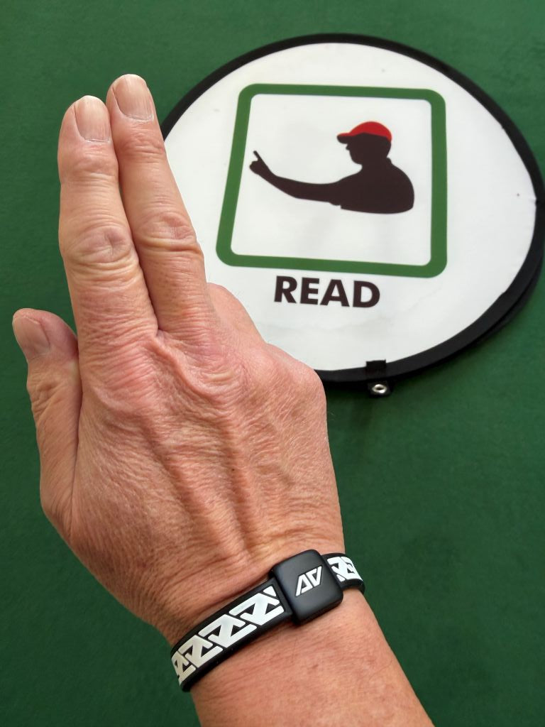Golf coach Mark Bentley wearing the AV Edge Legend White/Black frequency wristband while indicating a 'read' sign, demonstrating how the HEF Technology might support mental focus, green-reading clarity, and balance during instructional sessions, providing a non-invasive tool for peak coaching concentration.