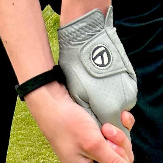 Close-up of Welsh junior golfer Alfie Dacey's gloved hand holding a club, wearing his all-black AV Edge Legend Noir frequency wristband, demonstrating how the HEF Technology might support enhanced golf performance, focus, and stability for developing competitive athletes