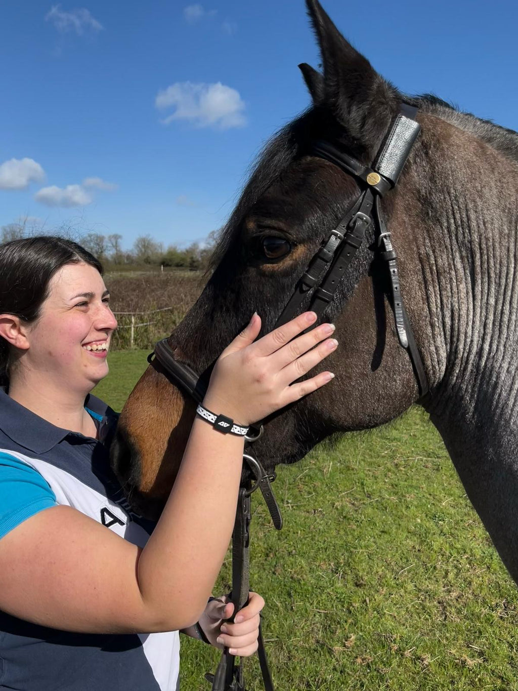 AV Edge advocate Paige Roberts wearing the Legend White/Black frequency wristband while smiling and petting her horse, demonstrating how HEF Technology might support rider focus and emotional well-being while providing a non-magnetic solution for natural EMF protection.